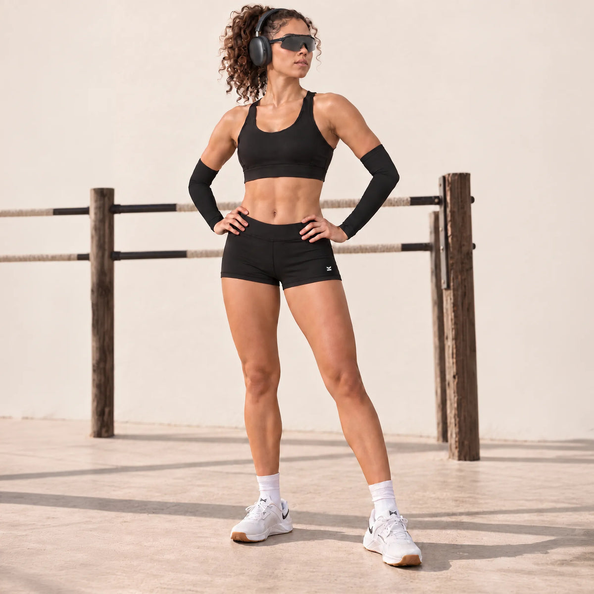 Top deportivo ASTRA de VALTIK en color Ónix, vista frontal en modelo de cuerpo completo con las manos en la cintura.